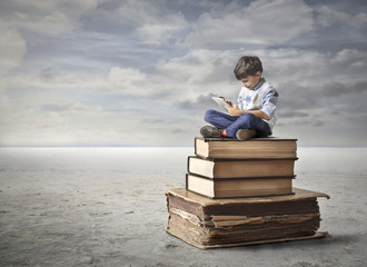 Un petit garçon assis sur une pile de livres, dont certains très anciens, symbolise la transmission de l’histoire familiale au fil des générations.
